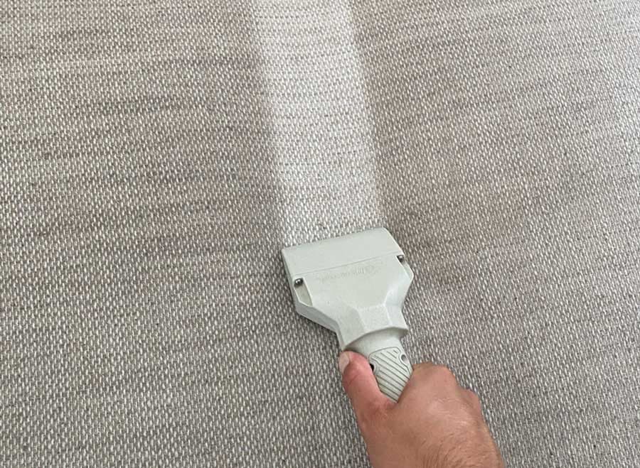 Upholstery tool cleaning a light woven rug, showing the clean stripe